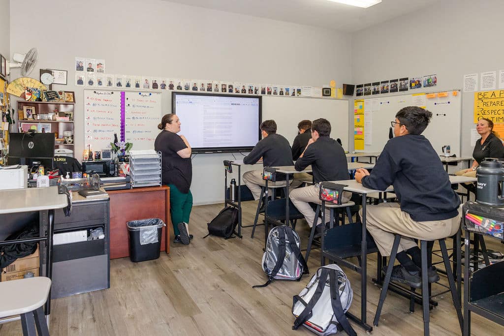 teacher stands before students at their desks in a classroom