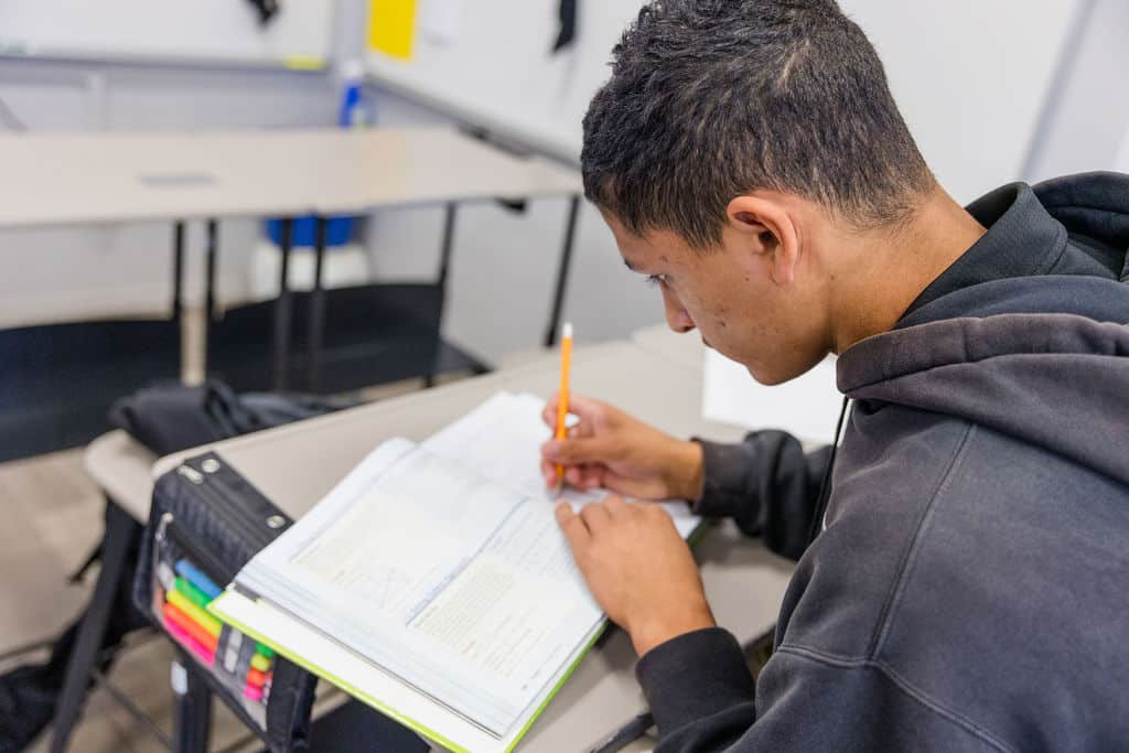 A young male student is writing in a notebook, immersed in his studies