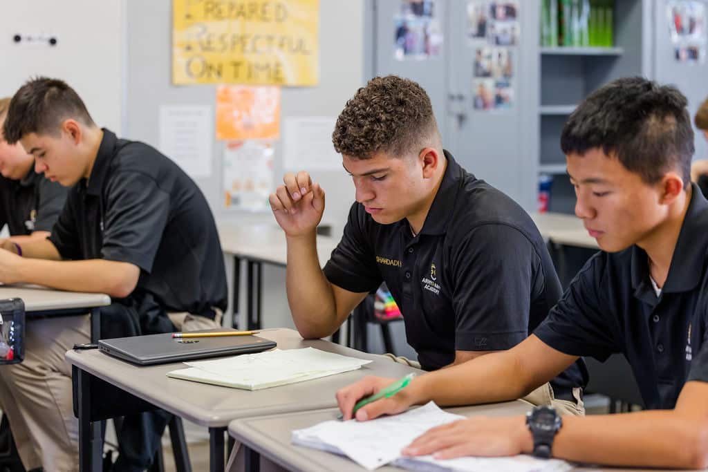 Students in a classroom sitting at desks in focused poses, writing on papers.