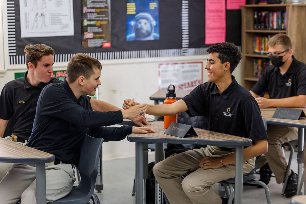 Four students in uniform sit at desks in a classroom.