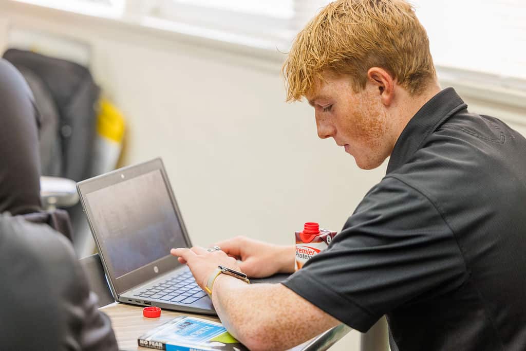 A young man wearing a black shirt, sits at a desk, focused on his computer