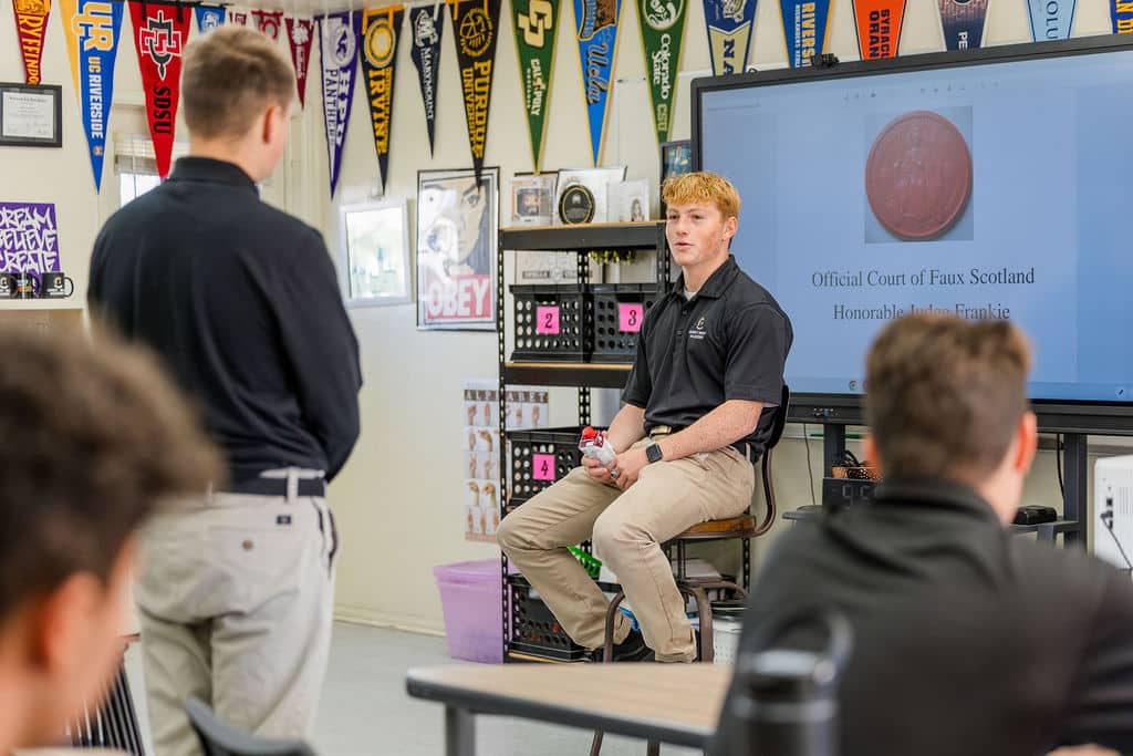 classroom setting with a student standing and another student sitting on a stool in front of a presentation screen