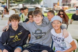 Three young men sitting together, smiling and enjoying a casual outdoor setting.