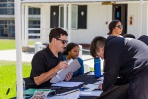 Students and staff interacting at an outdoor check-in table during move-in day.