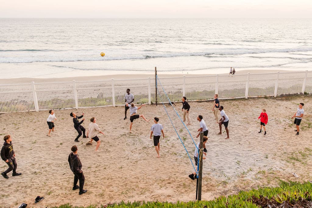 A group of people enjoying a game of beach volleyball on a sandy court by the ocean.