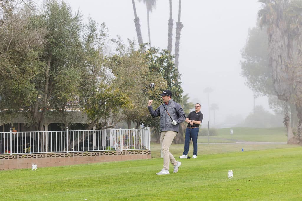 man stands in an open field, golf club in hand, preparing to play a round of golf