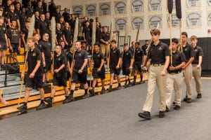 Students in uniform march in formation inside a gymnasium during school year opening